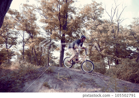 Young man in helmet training outdoors in forest, riding bmx bike, doing tricks. Autumn ride, extreme man 105502791