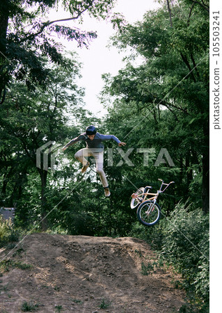 Dangerous ride. Young active man riding bmw bike outdoors in forest, park, training and doing difficult tricks in the air during ride Dangerous ride. Young active man riding bmw bike outdoors in forest, park, training and doing difficult tricks in the air during ride 105503241