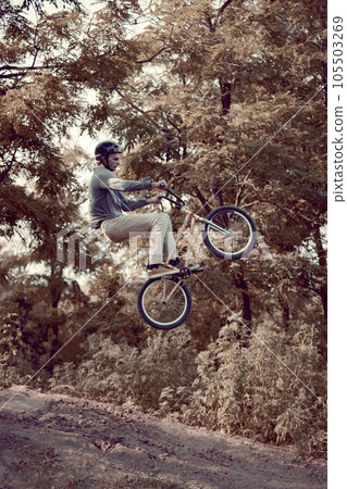Young man training riding bmx bike outdoors in park with special roads for extreme riding. Strength and endurance 105503269