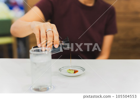 Woman customer hand pouring Japanese soy sauce on wasabi in small plate. 105504553