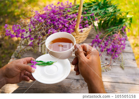 Close-up of men's hands with a white cup of tea. Healthy organic leaves Ivan chai tea Russian herbal on the wooden table 105505158