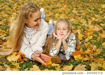 The Caucasian family has fun in the park. The girl and mother lie on a blanket. Mother looks at her daughter and smiles The Caucasian family has fun in the park. The girl and mother lie on a blanket. Mother looks at her daughter and smiles 105505719