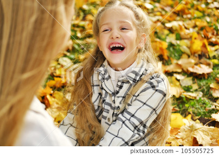 The Caucasian family has fun in the park. The girl and mother sit on a blanket and rest. The girl looks at her mother and laughs 105505725