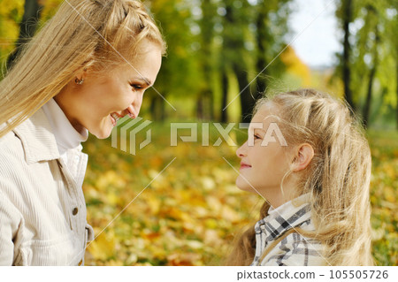 The family has fun in the park. Girl and mother sit opposite each other and smile 105505726