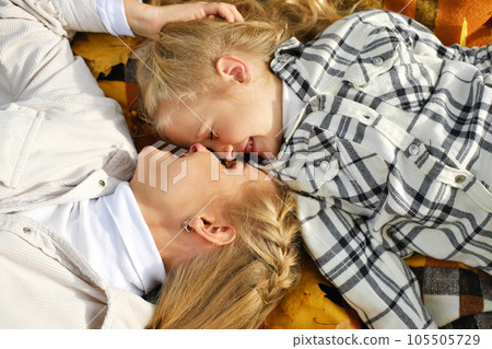 The family has fun in the park. Girl and mother lie on a blanket with eyes closed from happiness 105505729
