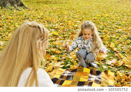 The family has fun in the park. Girl and mother spread a plaid on an autumn meadow The family has fun in the park. Girl and mother spread a plaid on an autumn meadow 105505752