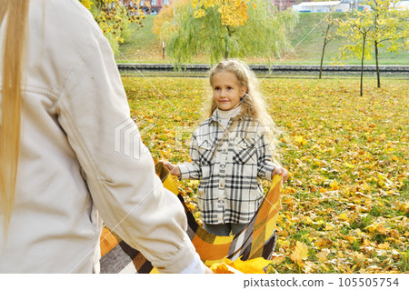The family has fun in the park. Girl and mother spread a plaid on an autumn meadow The family has fun in the park. Girl and mother spread a plaid on an autumn meadow 105505754