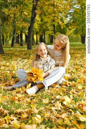 The family has fun in the park. Girl and mother sit on the ground among yellow leaves and fool around The family has fun in the park. Girl and mother sit on the ground among yellow leaves and fool around 105505761