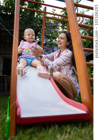 little baby girl with mother on slide in playground little baby girl with mother on slide in playground 105506203
