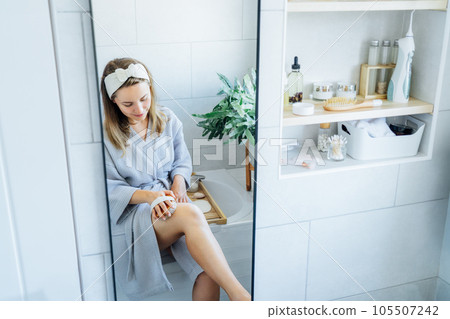Young woman in bathrobe doing scrubbing massage with dry brush before morning shower in light colored bathroom. Anti-cellulite treatment, lymphatic drainage massage. Women beauty. Selective focus 105507242