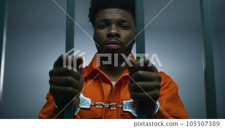 Man keeps hands in handcuffs on jail cell bars Man keeps hands in handcuffs on jail cell bars 105507389