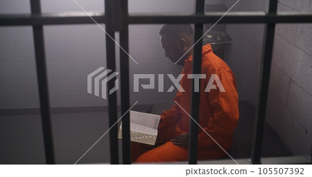 African American prisoner sits in prison cell, reads Bible African American prisoner sits in prison cell, reads Bible 105507392