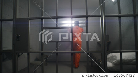 Prisoner in orange uniform looks at barred window Prisoner in orange uniform looks at barred window 105507428