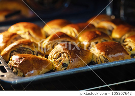 Freshly baked homemade buns with poppy seeds and raisins lie on a baking sheet Freshly baked homemade buns with poppy seeds and raisins lie on a baking sheet 105507642