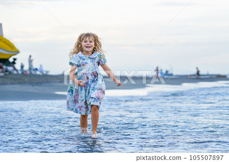 Happy Child, Little Preschool Girl in Dress Running And Jumping In The Waves During Summer Vacation On Exotic Tropical Beach by Sunset. Family Journey On Ocean Coast. 105507897