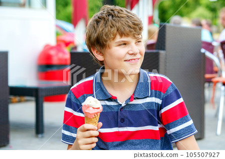 Cheerful laughing preteen boy eating multicolored ice cream in a waffle cone. Cool in the summer heat.Sweet snack for children. Happy child. Cheerful laughing preteen boy eating multicolored ice cream in a waffle cone. Cool in the summer heat.Sweet snack for children. Happy child. 105507927
