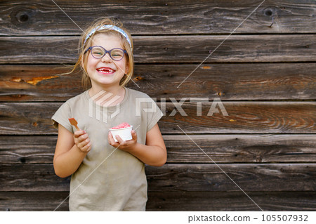Little adorable preschool girl with eyeglasses eating berry and watermelon ice cream sundae in cup on sunny summer day. Happy child eat icecream dessert. Sweet food on hot warm summertime days Little adorable preschool girl with eyeglasses eating berry and watermelon ice cream sundae in cup on sunny summer day. Happy child eat icecream dessert. Sweet food on hot warm summertime days 105507932