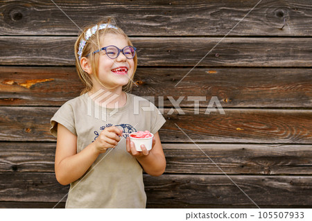 Little adorable preschool girl with eyeglasses eating berry and watermelon ice cream sundae in cup on sunny summer day. Happy child eat icecream dessert. Sweet food on hot warm summertime days Little adorable preschool girl with eyeglasses eating berry and watermelon ice cream sundae in cup on sunny summer day. Happy child eat icecream dessert. Sweet food on hot warm summertime days 105507933