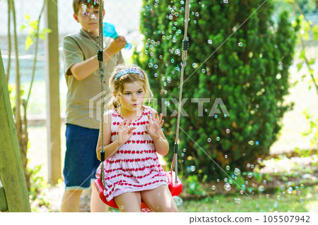 Happy little preschool girl and school kid boy having fun with blowing soap bubble blower. Children, lovely siblings playing together. Active funny healthy kids. Brother and sister in love. 105507942