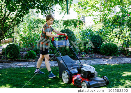 Happy preteen kid boy with lawn mower. Portrait of smiling teenager child working in garden, trimming grass. Garden works in summer. Kid helping 105508290