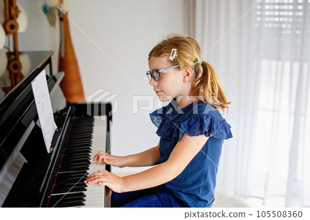 Beautiful little preschool girl playing piano at music school. Cute child having fun with learning to play music instrument. Early musical education for children 105508360