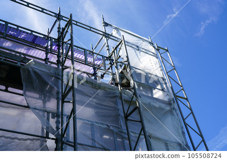 Modular scaffold construction frame with safety net around house facade on blue sky background 105508724