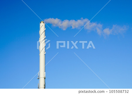 A tall white smoking chimney against a blue sky background A tall white smoking chimney against a blue sky background 105508732