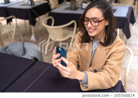Middle-aged woman using smartphone sitting outdoor cafe 105508814