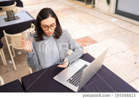 Freelancer using smartphone and laptop sitting outdoor cafe drink water 105508815