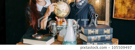 Two schoolgirls perform chemical experiments. Flasks with solutions and chemical formulas on the blackboard in the school classroom. 105509497