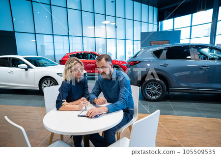 Caucasian couple signs a car purchase agreement in a car dealership.  105509535