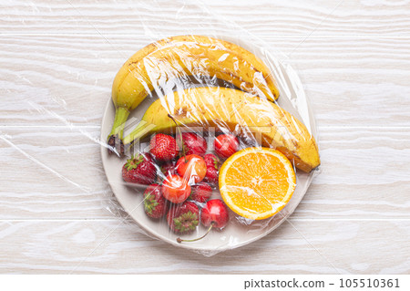Assorted different fruit and berries on white plate wrapped in plastic clear film top view on white wooden rustic table background Assorted different fruit and berries on white plate wrapped in plastic clear film top view on white wooden rustic table background 105510361