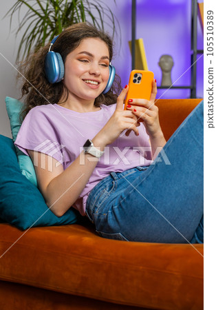 Happy young woman in wireless headphones relaxing lying on sofa at home listening favorite music 105510389