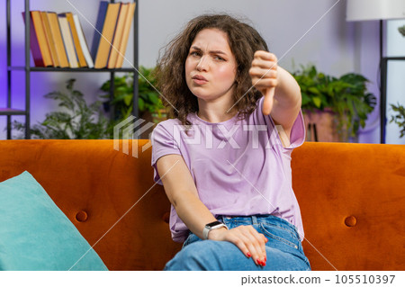 Upset young woman showing thumbs down, dislike bad work, disapproval, dissatisfied feedback at home 105510397