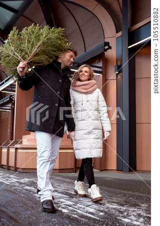 Beautiful young couple in love buying a Christmas tree from the market to decorate their home. Caucasian man and woman are preparing for Christmas. Anticipation of the New Year Eve in a snowy city. Beautiful young couple in love buying a Christmas tree from the market to decorate their home. Caucasian man and woman are preparing for Christmas. Anticipation of the New Year Eve in a snowy city. 105510882