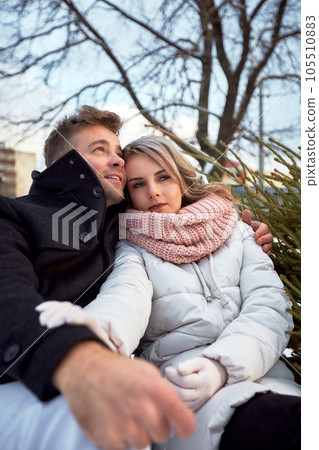 Happy couple in love in Christmas market. Young beautiful man and woman in winterwear embracing and looking dreamily into the distance. Romantic outside dating in winter snowy city. Happy couple in love in Christmas market. Young beautiful man and woman in winterwear embracing and looking dreamily into the distance. Romantic outside dating in winter snowy city. 105510883