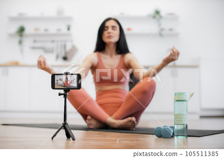 Lady recording video while meditating in lotus position Lady recording video while meditating in lotus position 105511385