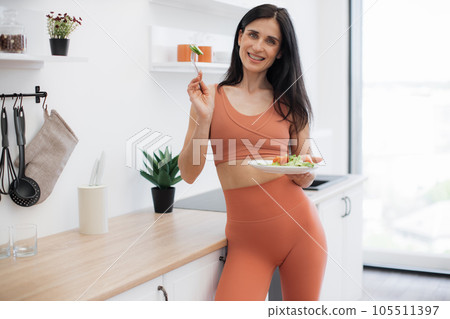 Skinny lady leaning on kitchen surface with salad in hands 105511397