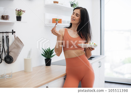 Skinny lady leaning on kitchen surface with salad in hands 105511398