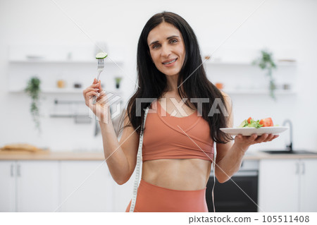Active woman smelling fresh vegetables after workout at home Active woman smelling fresh vegetables after workout at home 105511408