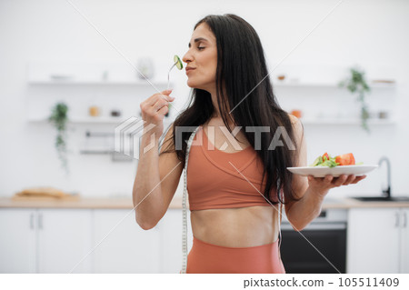 Active woman smelling fresh vegetables after workout at home 105511409