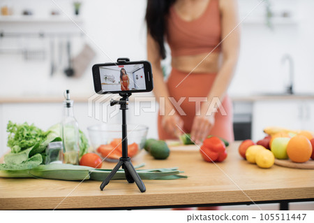 Female blogger cutting cucumber on phone camera at home 105511447