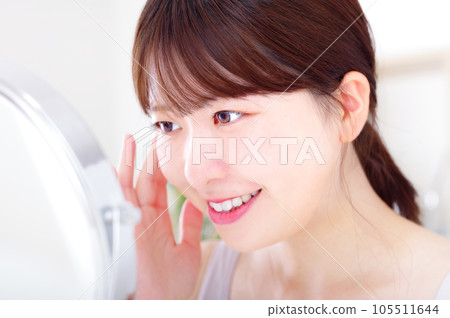 Young woman doing facial skin care while looking in the mirror Young woman doing facial skin care while looking in the mirror 105511644