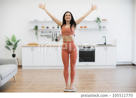 Lady on scales raising arms in victory gesture at home 105511770