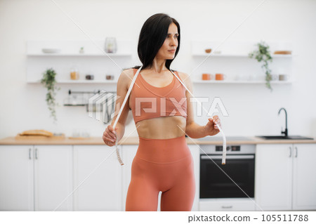 Sportswoman stretching measuring tape on shoulders at home Sportswoman stretching measuring tape on shoulders at home 105511788