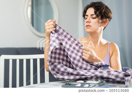 Young woman sitting at table and enjoying process of sewing clothes. Satisfied with work done Young woman sitting at table and enjoying process of sewing clothes. Satisfied with work done 105513080