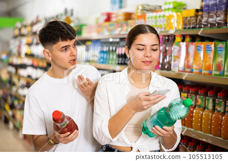 in shop, man and woman chooses drink. Girl scans QR code from label on water in shop, man and woman chooses drink. Girl scans QR code from label on water 105513105