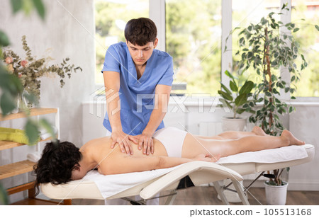 Male masseur doing massage at back young woman who lying on massage table in beauty salon Male masseur doing massage at back young woman who lying on massage table in beauty salon 105513168