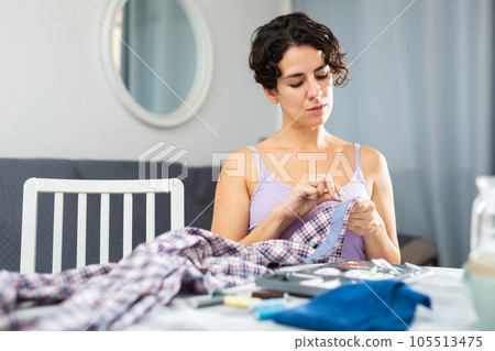 Portrait of attractive focused female using needle and thread to sew shirt Portrait of attractive focused female using needle and thread to sew shirt 105513475