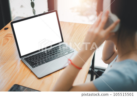 Close-up back view of a woman working on notebook computer and using headphone, looking at the screen. office worker using a notebook computer.. 105515501
